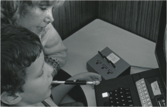 Photo of Sheryl with 6-year old Rodney at the computer with a switch box